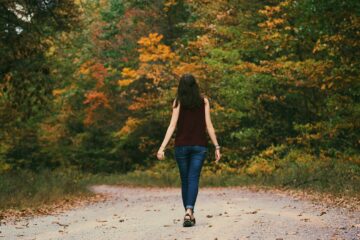 Woman in Brown Sleeveless Dress and Blue Jeans Standing on Gray Path Road